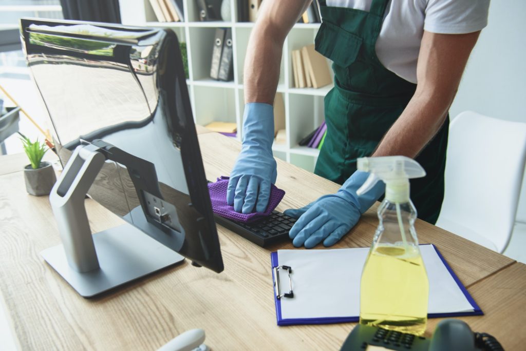 cropped shot of professional cleaner in rubber gloves cleaning computer keyboard in office